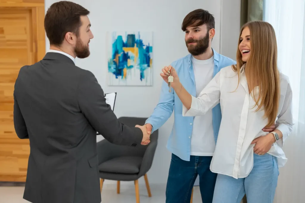 A happy couple receiving keys to their new home from a real estate agent.