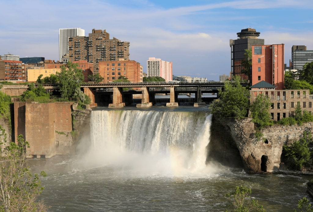 A waterfall flowing through an urban landscape, featuring buildings and a bridge situated above the water.