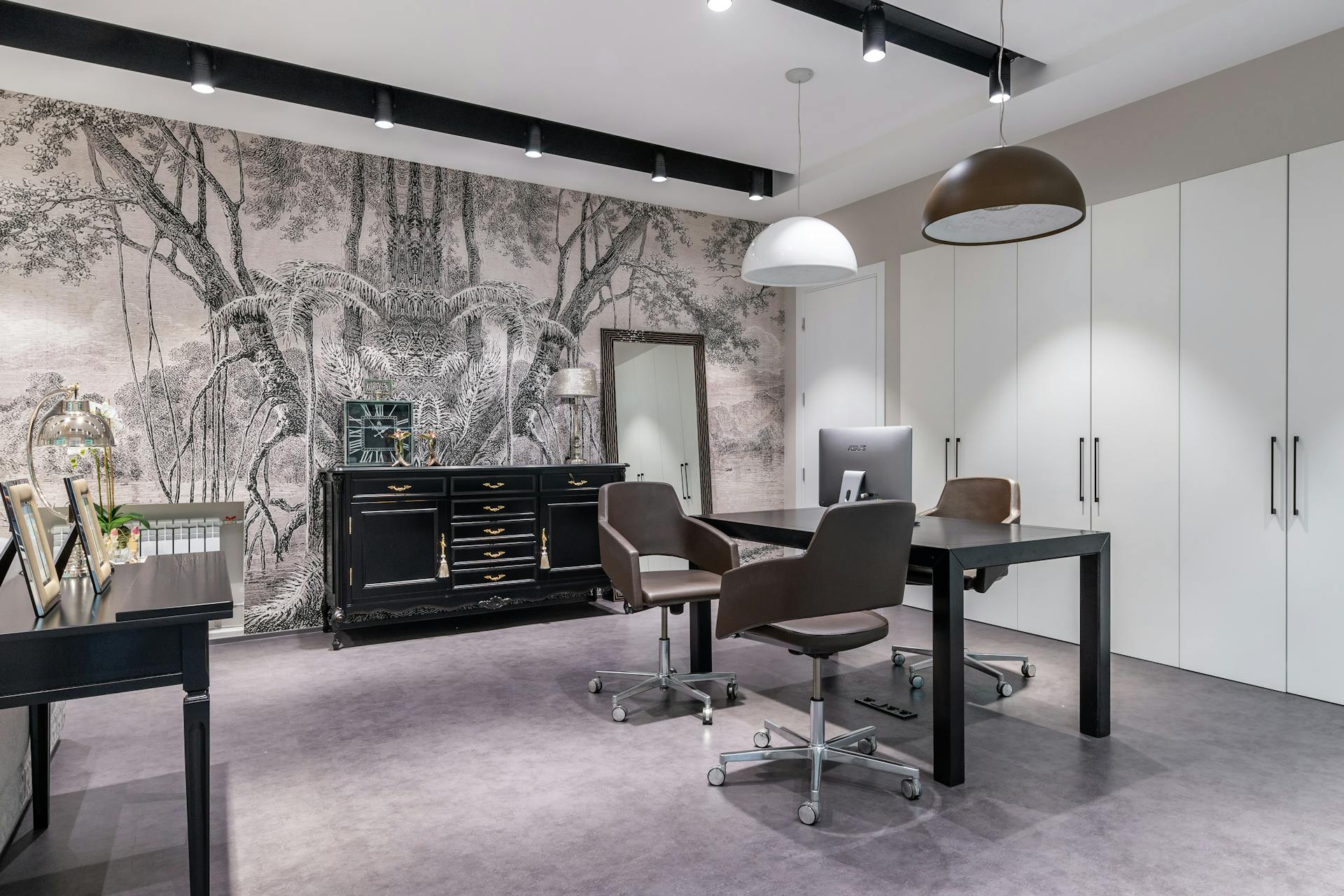 A stylish, modern home office featuring a black desk, brown swivel chairs, white cabinets, and a decorative mural wall.